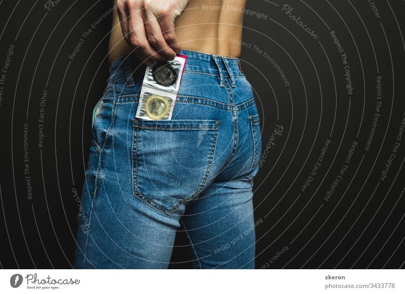 junger Typ in Jeans bereitet sich auf ein romantisches Date vor - gibt ein farbiges Kondom in die Gesäßtasche seiner Jeans. Körperteil: männlicher Arsch. Konzept: Schutz vor sexuell übertragbaren Krankheiten