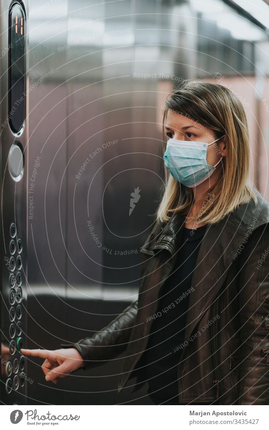Junge Frau mit medizinischer Maske im Aufzug eines Wohnhauses Erwachsener Biogefährdung Pflege Kaukasier Coronavirus COVID19 krisen Gefahr Krankheit
