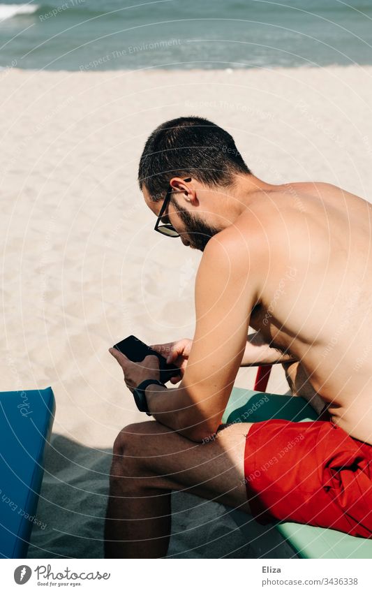 Gestrandeter Urlauber sitzt am Strand und ist mit seinem Smartphone beschäftigt gestrandet Corona Covid-19 Reisen Tourist gestresst besorgt Stress