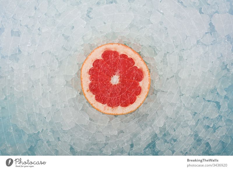 Frische rosa Grapefruitscheibe über zerstoßenem Eis rot eine Hälfte geschnitten Scheibe frisch zerdrückt Hintergrund Nahaufnahme blau weiß kalt gefroren Frucht