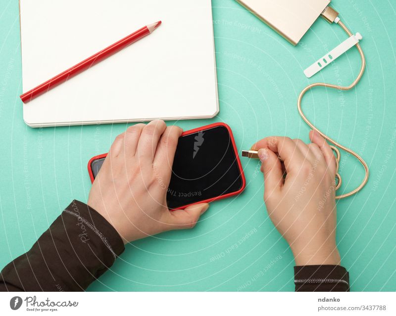 zwei Hände, die ein rotes mobiles Smartphone und ein Ladekabel auf grünem Hintergrund halten Adapter Erwachsener Kabel Kaukasier Funktelefon Gebühr Ladegerät