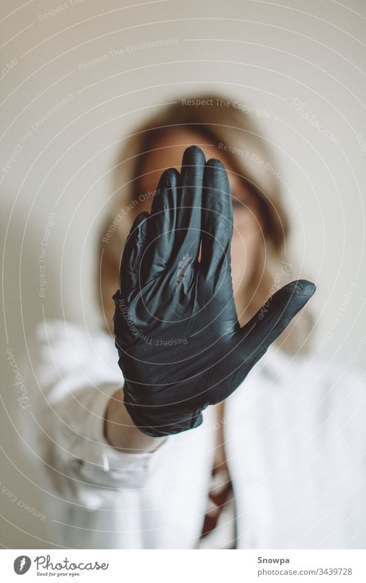 Frau zeigt Stoppschild mit schwarzem Handschuh Handschuhe schwarze Handschuhe Gummihandschuh Arzt Wissenschaftler blond blondes Haar bürsten covid-19