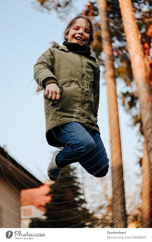 Kleines Mädchen im Flug, sie hüpft auf einem Trampolin im Garten vor zwei Kiefern klein Kind Schulkind hüpfen springen fliegen Freude Spielen Kindheit