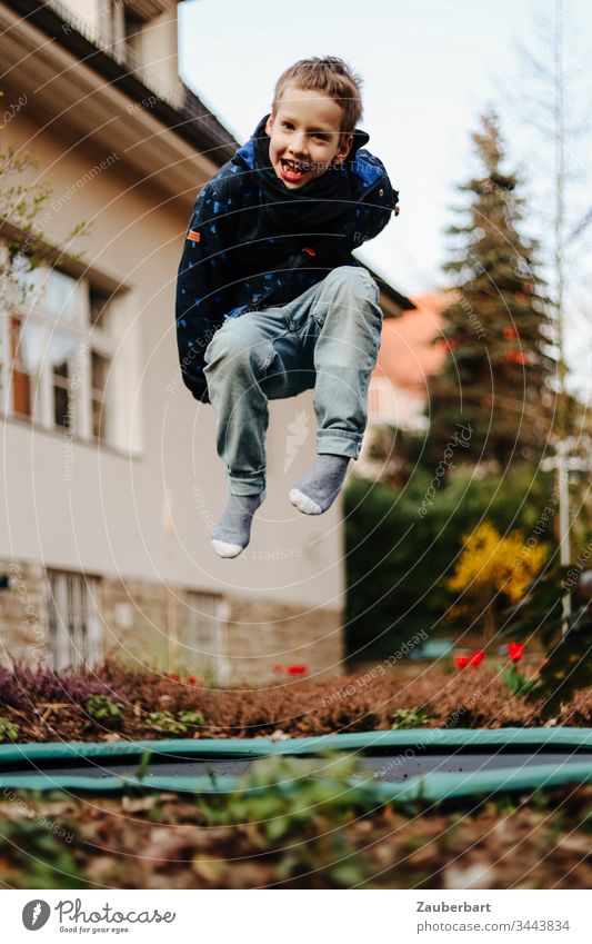 Kleiner Junge lacht und hüpft auf einem Trampolin im Garten eines Hauses klein Kind Schulkind hüpfen springen fliegen Villa Heidekrautgewächse Freude Spielen