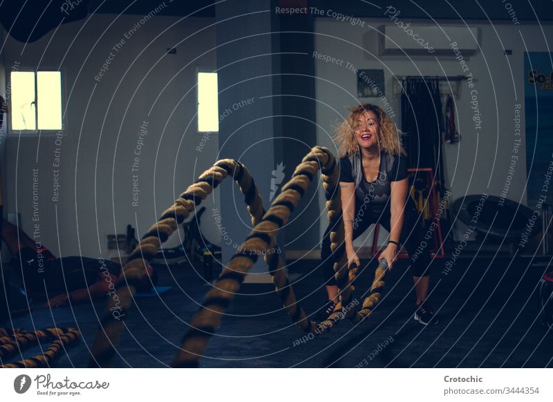 Blonde Frau benutzt das Kampfseil in einer Turnhalle Fitnessstudio Sport Schlacht Seil Aerobic Athlet Club Tatkraft anstrengen Ausdauer Übung passen Kunstturnen