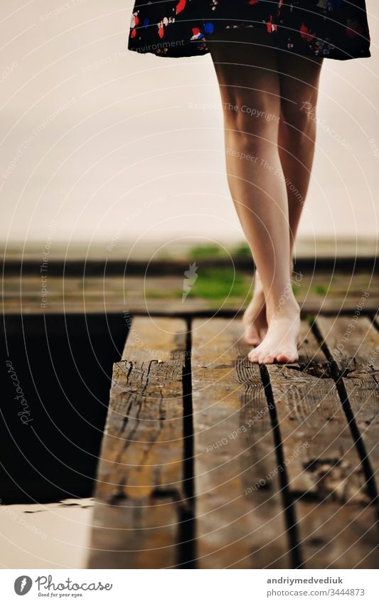 Ein Mädchen geht auf einer Holzbrücke zum See. Die Brücke auf dem See. Wunderschön barfuß. allein Sommer Beine Lifestyle aktiv Hintergrund Barfuß Strand Körper