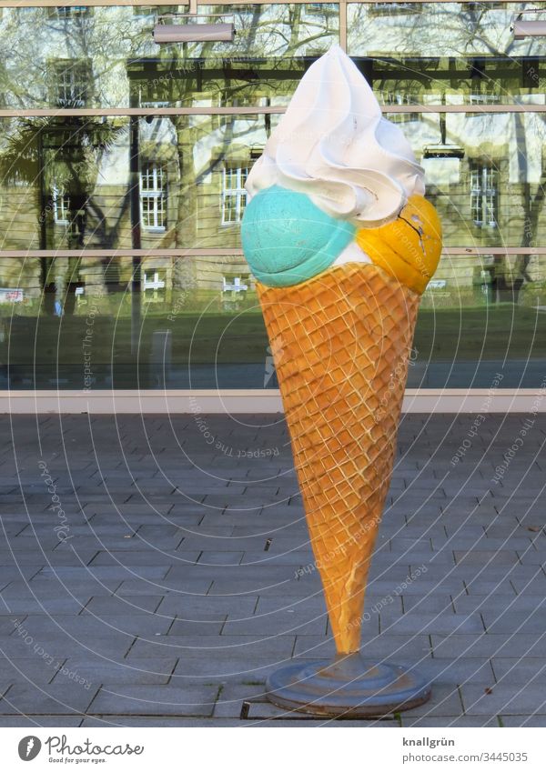 Eiscreme Werbung in Form eines überdimensionalen Waffelhörnchens mit einer pistaziengrünen und einer mangogelben Eiskugel mit Schlagsahne obendrauf Süßigkeiten
