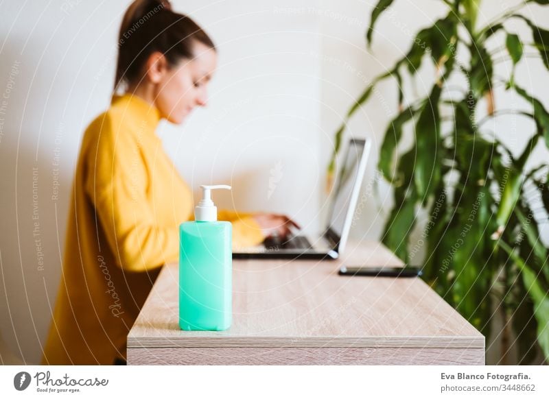 junge Frau, die zu Hause am Laptop arbeitet und Handdesinfektionsmittel Alkoholgel verwendet. Während des Coronavirus covid-2019-Konzepts zu Hause bleiben