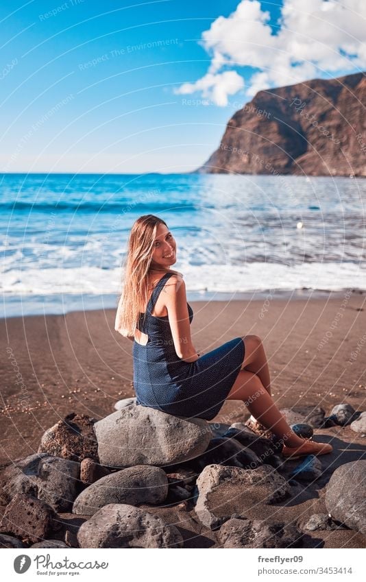Junge Frau am Strand von Los Gigantes auf Teneriffa, Kanarische Inseln, Spanien allein atlantisch Hintergrund zurück Schönheit blond blau Klippe Küste