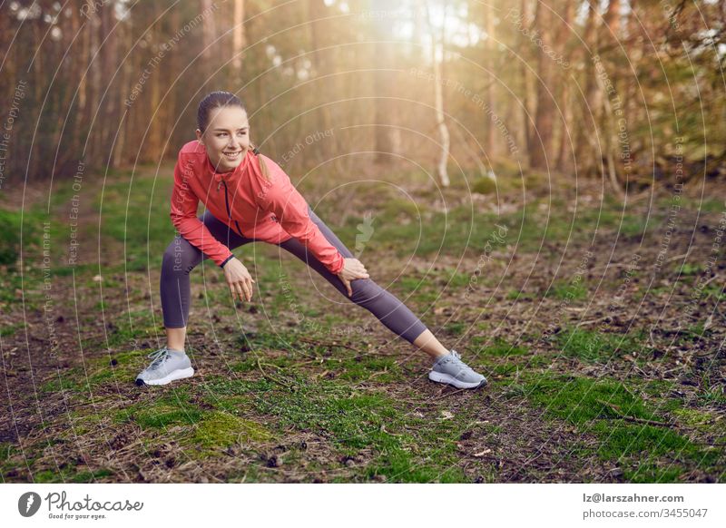 Ganzfigur einer fröhlich-fröhlichen jungen Frau, die während des Trainings im Wald im Frühling Dehnungsübungen für Beine und Arme macht Glück selbstbewusst