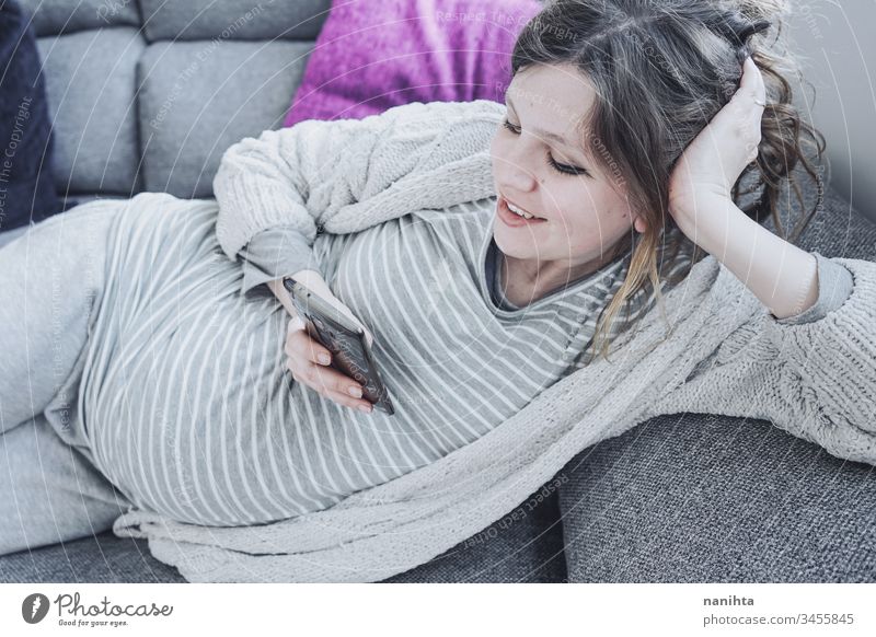 Junge schwangere Frau zu Hause mit ihrem Mobiltelefon Mama Arbeit Telefon heimwärts Quarantäne Schwangerschaft sich[Akk] entspannen Technik & Technologie Job