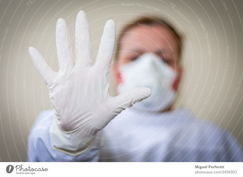 Krankenschwester mit Schutzmaske und ausgestreckter Hand mit Handschuh, die rät, den Sicherheitsabstand einzuhalten, um sich nicht zu infizieren, auf beigem Hintergrund