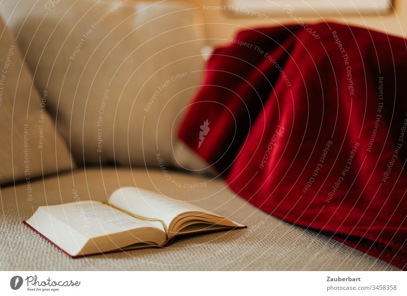 Buch liegt auf gemütlicher Couch mit roter Decke stayhome lesen aufgeschlagen beige Erholung stay at home ruhen Geborgenheit Rückzug kontemplativ Lifestyle