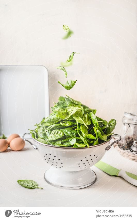 Sieb mit Spinat und fallenden Spinatblättern auf weißem Küchentisch. Konzept für gesunde Ernährung Blätter Tisch lecker Schalen & Schüsseln Haufen Gesundheit