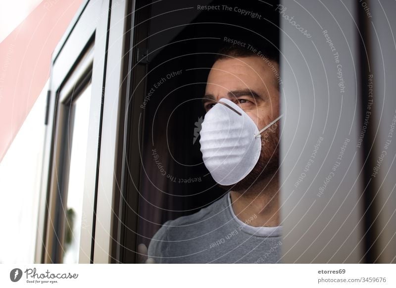 Mann mit Gesichtsmaske und Handschuhen, der aus dem Fenster schaut Coronavirus Virus Quarantäne covid-19 Mundschutz Einsperrung Einwegartikel zu Hause bleiben