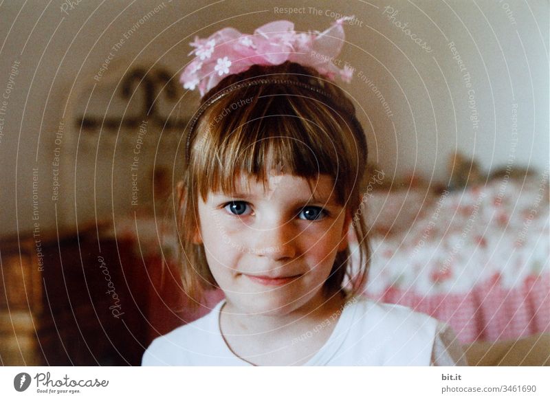 Kleines Mädchen freut sich glückselig über ihren Haarschmuck aus rosa Blumen und ist verkleidet als Prinzessin mit Krone aus Blüten. mädchenhaft Mädchenportrait