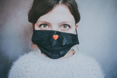Junge Frau trägt eine Maske mit einem roten Herz Bund 19 COVID Coronavirus Virus Atem Pandemie Mundschutz Krankheit Hoffnung Liebe Hilfsbereitschaft Solidarität