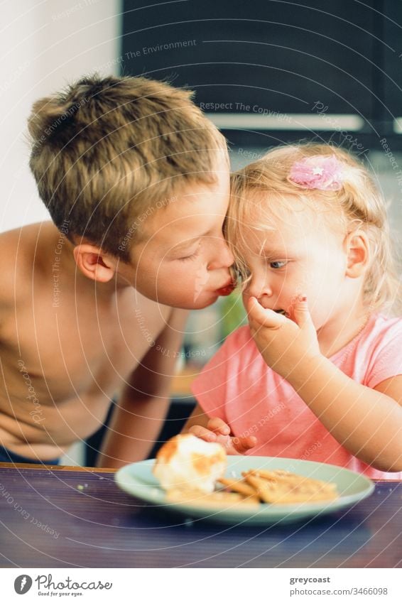Er kümmert sich immer um die kleine Schwester und liebt sie sehr. Brüder küssen für Mädchen während des Frühstücks Kinder Liebe Kuss Wange Bruder Geschwister