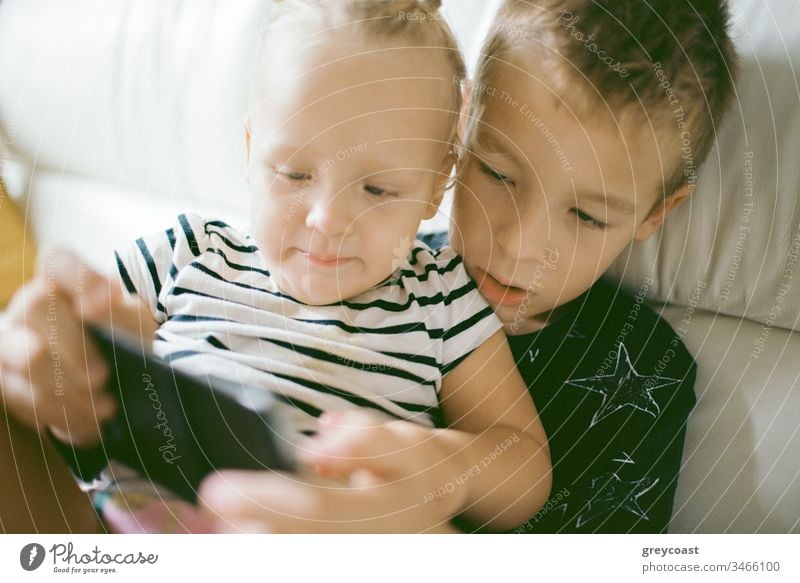 Kinder verbringen ihre Freizeit zu Hause mit Handyspielen. Großer Bruder passt auf kleine Schwester auf und hilft ihr beim Spielen Mobile Spaß heimwärts