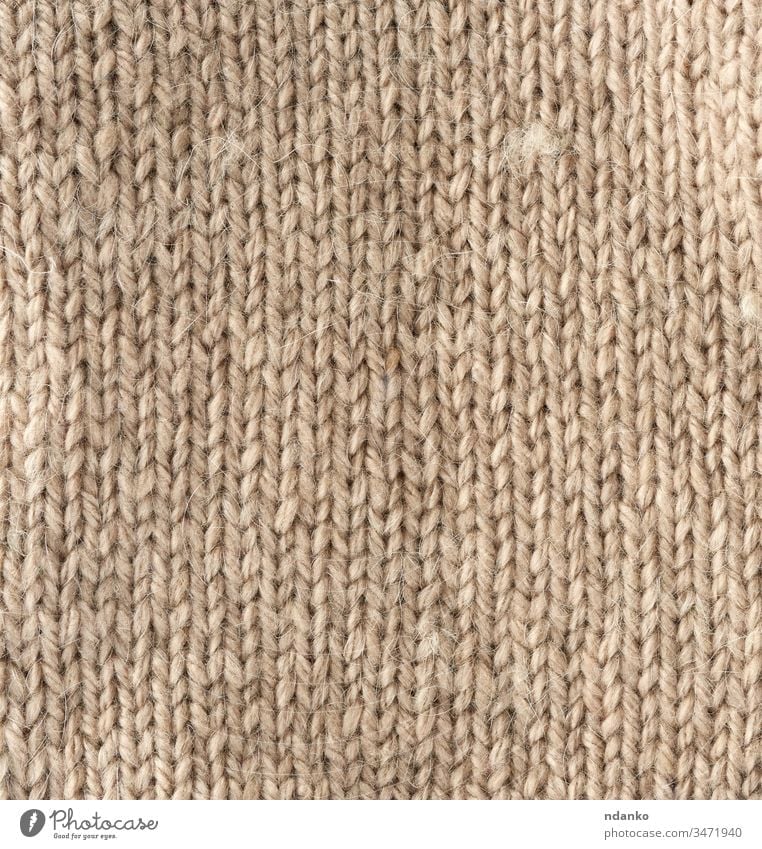 Fragment einer Maschenware aus hellbrauner Schafwolle beige Garn Hintergrund Leinwand Nahaufnahme Stoff Kleidung Bekleidung Farbe Handwerk Dekor dekorativ