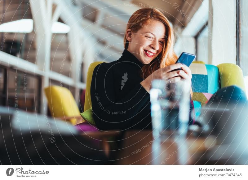 Junge glückliche Frau benutzt Smartphone in einem Cafe jung Glück Lächeln Café im Innenbereich lässig Tisch Sitzen Lifestyle verbunden Anschluss Mobile Telefon