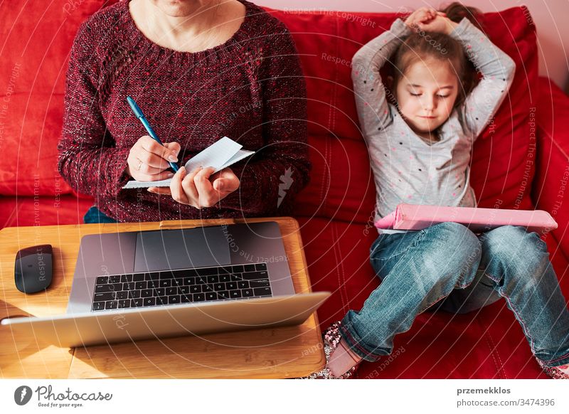 Mutter einer Frau, die während der COVID-19-Quarantäne von zu Hause aus per Video-Chat-Call-Stream-Online-Kurs Webinar auf einem Laptop durchführt, während ihre Tochter sich ein Video auf einem Tablet anschaut. Frau sitzt im Bett vor dem Computer und schaut auf den Bildschirm
