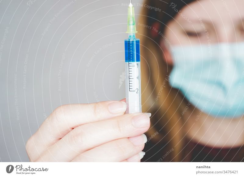 Junge Frau trägt eine Gesichtsmaske und hält einen Impfstoff Bund 19 COVID Grippe Mundschutz Coronavirus Pandemie Seuche Erkundung Atelier Behandlung Medizin
