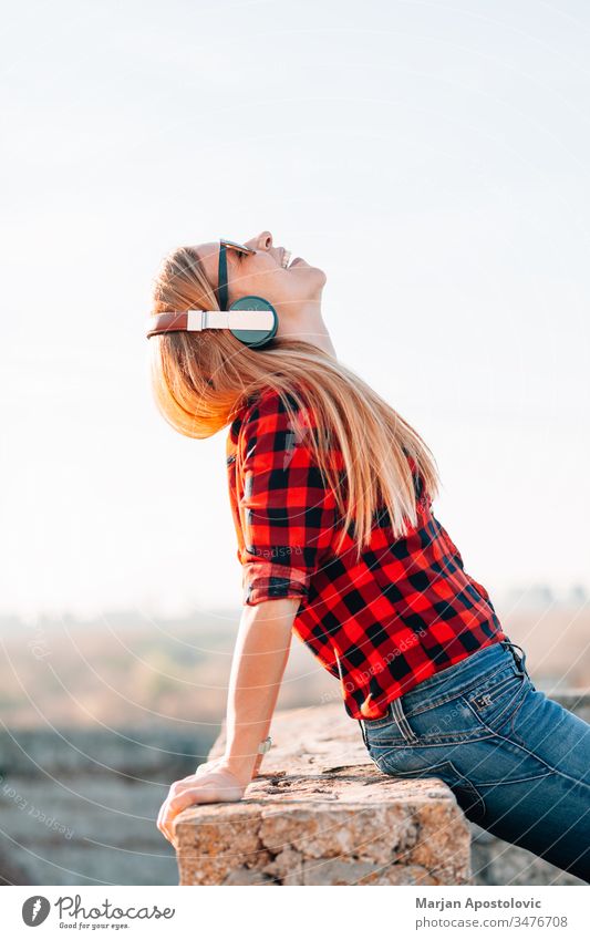 Junge Frau, die bei Sonnenuntergang im Freien mit Kopfhörern Musik hört jung hören außerhalb genießend Freude freudig Drahtlos Technik & Technologie lässig