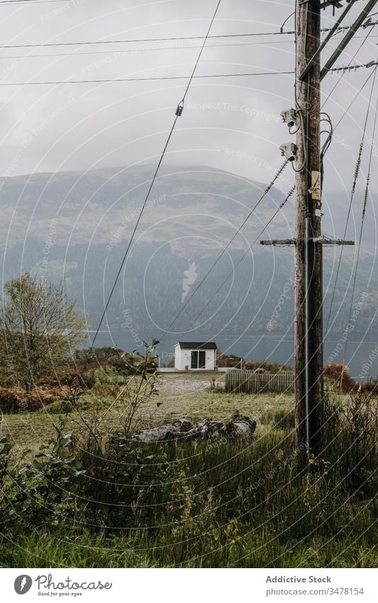 Einsames Haus am Seeufer in bergigem Gelände mit elektrischen Kabeln Landschaft Berge u. Gebirge Mast bedeckt Nebel ländlich Schottland trist Cottage Ufer