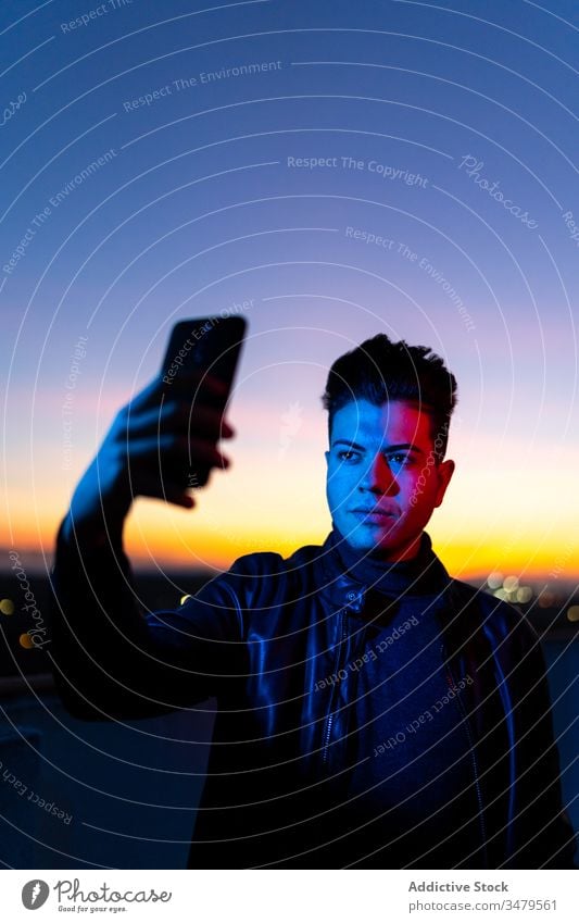 Junger Mann nimmt sich abends selbst die Zeit Smartphone Selfie neonfarbig Handy Sonnenuntergang dunkel blau Licht Himmel Stil ernst Farbe Apparatur Gerät