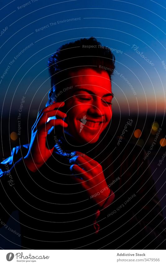 Hübscher Kerl telefoniert auf nächtlicher Straße Mann neonfarbig Smartphone reden dunkel rot blau modern Nacht Gerät leuchten Apparatur Mitteilung selbstbewusst