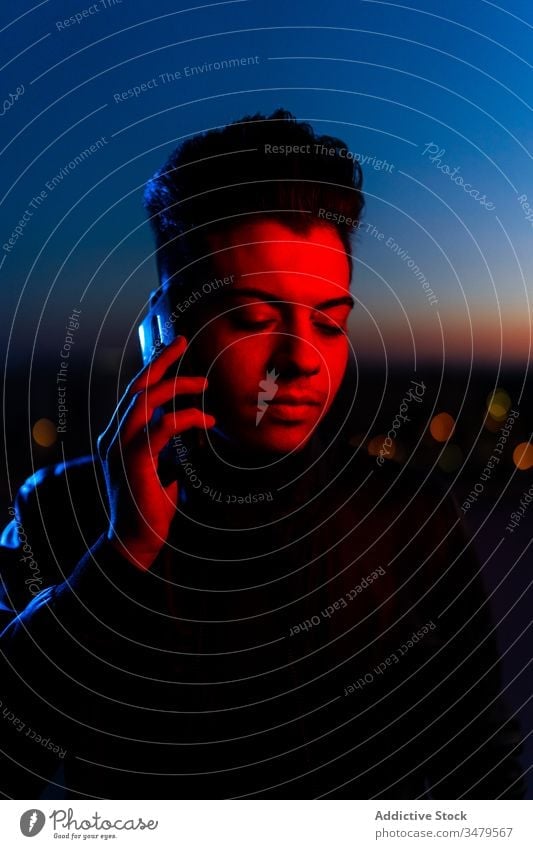 Hübscher Kerl telefoniert auf nächtlicher Straße Mann neonfarbig Smartphone reden dunkel rot blau modern Nacht ernst Gerät leuchten Apparatur Mitteilung