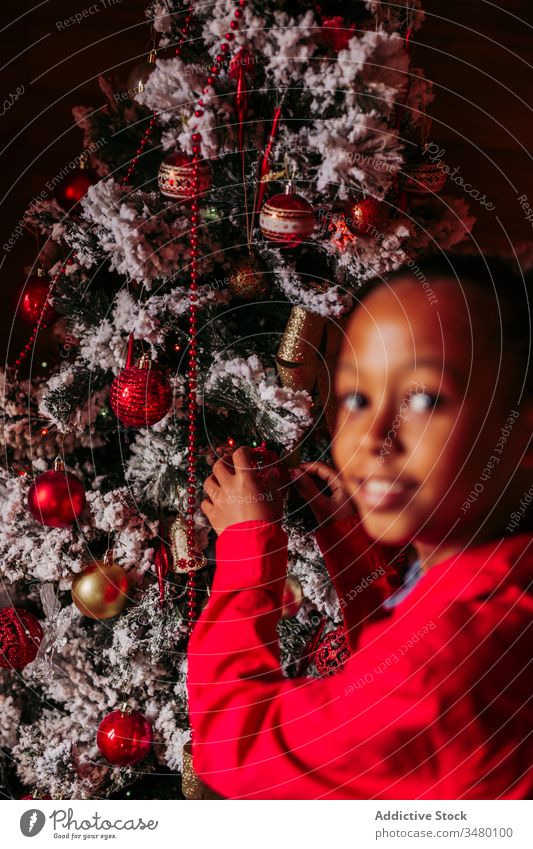 Glückliches kleines Mädchen schmückt den Weihnachtsbaum Kind Weihnachten Baum dekorieren Tradition heimwärts rustikal ethnisch Lächeln lässig heiter positiv