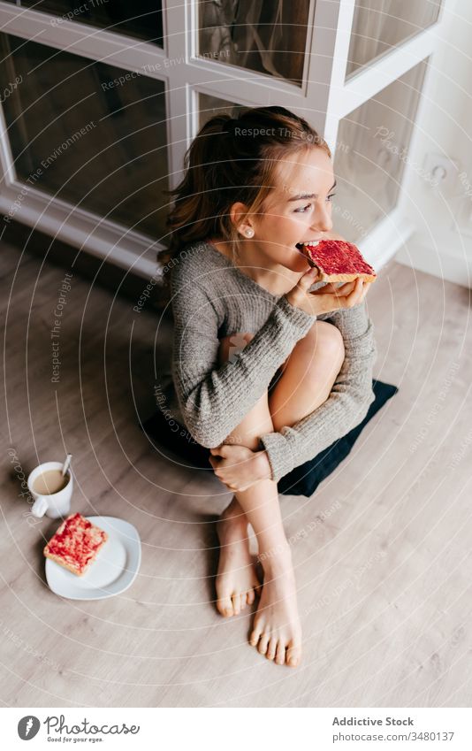 Junge Frau sitzt auf dem Boden und isst Frühstücks-Toasts heimwärts Zuprosten Kaffee Stock positiv lässig genießen Morgen essen süß Lächeln sich[Akk] entspannen