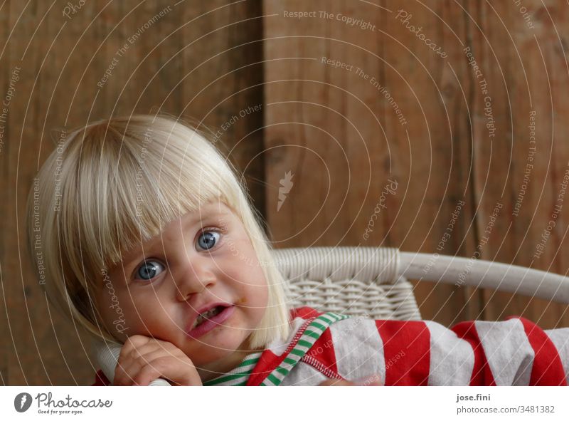 Kleines Mädchen sitzt auf einem Stuhl und schaut mit großen Augen in die Kamera Porträt Kind kleines Mädchen große Augen natürlich frech niedlich aufgeregt