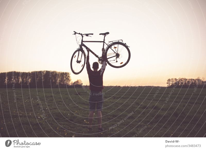 Mann hebt Fahrrad in die Luft Fahrradfahren Fahrradtour Liebe Natur Rad Naturerlebnis draußen gutes Wetter Feld hoch hochheben stark stärke Abenddämmerung