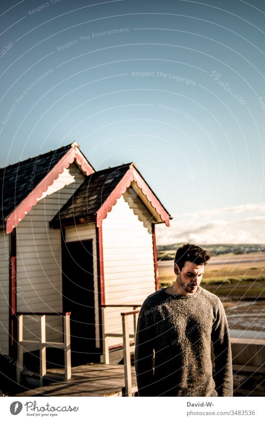 Mann an einem ruhigen Plätzchen in Skandinavien Holzhaus nachdenklich männlich maskulin gutes Wetter schön Sonnenlicht Blick nach unten Wegsehen Gedanken Model
