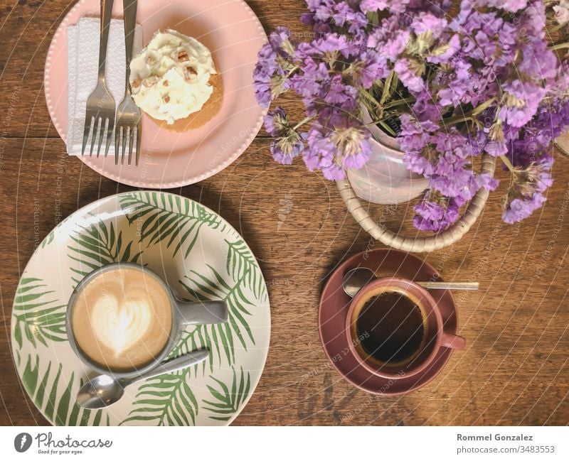 Tasse Cappuccino mit Latte Art und Xpresso auf einer Holzplatte und einem mit Trockenblumen dekorierten Holztisch, Selektiver Fokus, Weichzeichner Feier
