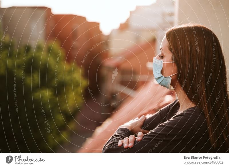 junge Frau zu Hause auf einer Terrasse, die eine Schutzmaske trägt und einen sonnigen Tag genießt. Coronavirus Covid-19-Konzept covid-19 schützend Mundschutz