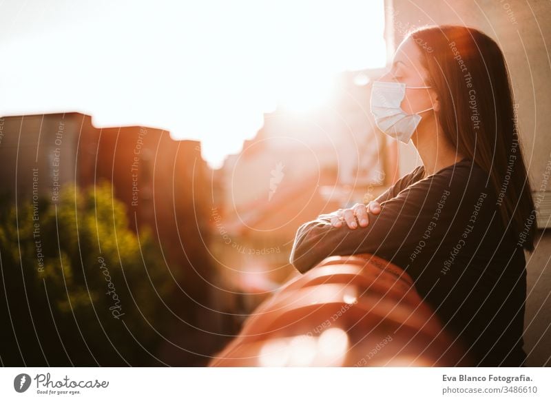 junge Frau zu Hause auf einer Terrasse, die eine Schutzmaske trägt und einen sonnigen Tag genießt. Coronavirus Covid-19-Konzept covid-19 schützend Mundschutz