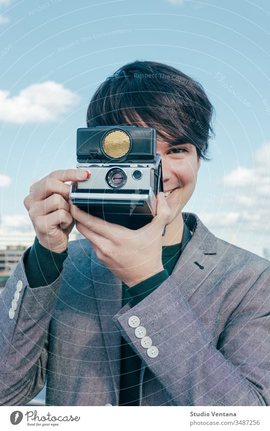 Junger gemischtrassiger Fotograf mit Polaroidkamera auf der Themse Lächeln altehrwürdig Business Tourist jung reisen Europa Ferien Sehenswürdigkeiten Himmel