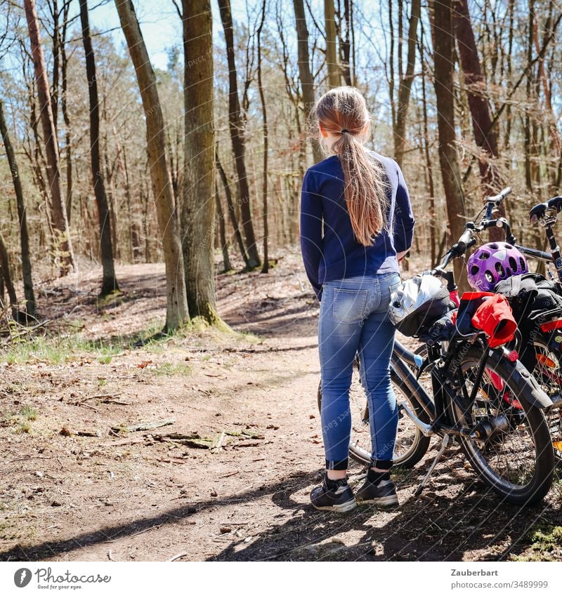 Kind mit Fahrrad steht bei einer Radtour auf einem Waldweg Mädchen Bäume Jeans Pferdeschwanz Sonne Kindheit Familie