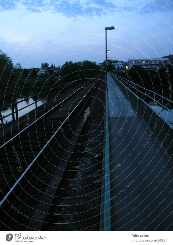 Zweigleisig Gleise Bürgersteig Laterne Straßenbeleuchtung Abzweigung parallel nebeneinander Eisenbahn Abendsonne Dämmerung Horizont Brücke Fluss Wasser Geländer