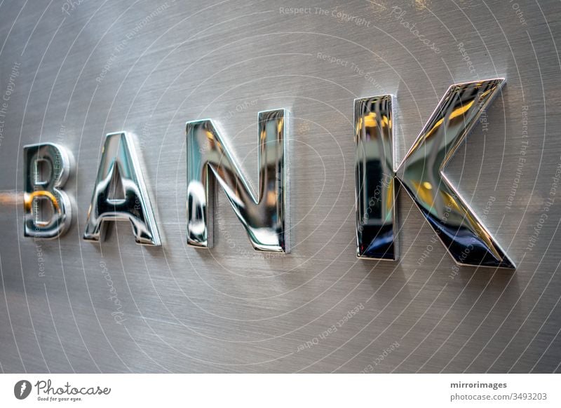Dreidimensionale Schrift BANK aus silber glänzendem Metall auf einer flachen Wandoberfläche aus gebürstetem Stahl Bankgebäude Bankwort Metall Banktyp