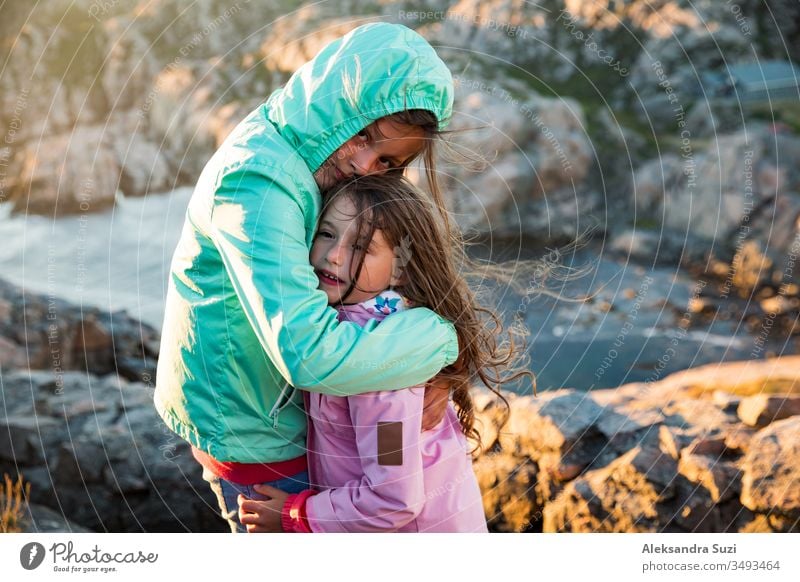 Zwei kleine Mädchen spielen an der felsigen nördlichen Meeresküste. stehen, lachen, umarmen, die Küstenfelsen erkunden. Reisen und ein großes Abenteuer in Norwegen erleben. Wunderschöne Aussicht auf Fjord und Berge bei Sonnenuntergang.