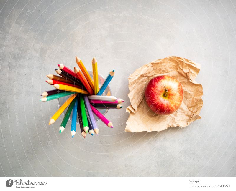 Draufsicht von Farbstiften und einem roten Apfel auf einem Backpapier, Bildung, Kunst, grauer Schultisch farbstift apfel drehen Schule kunst kreativ pausieren