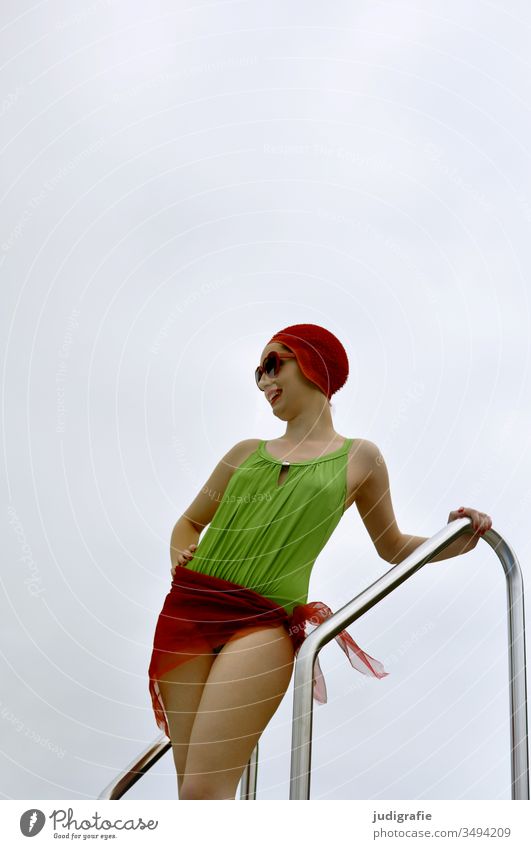 Das Mädchen mit der schönen roten Badekappe und dem grünem Badeanzug steht mit roter Sonnenbrille am Schwimmbeckenrand. Eine Sommerliebe. Frau Badebekleidung