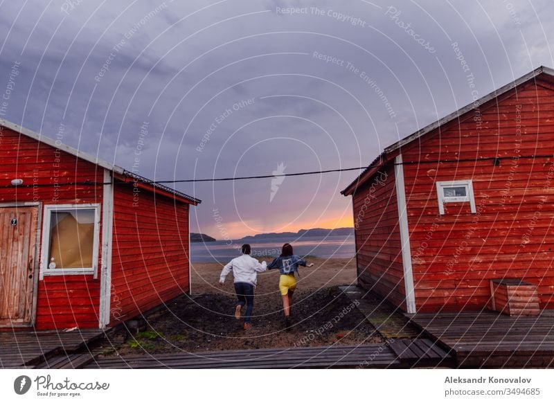 Junges Paar rennt auf dem Weg zur Barentssee auf nassem Sand in einem Sonnenuntergang am Polartag Meer Tundra polar Dorf Jeanshose Berge u. Gebirge laufen