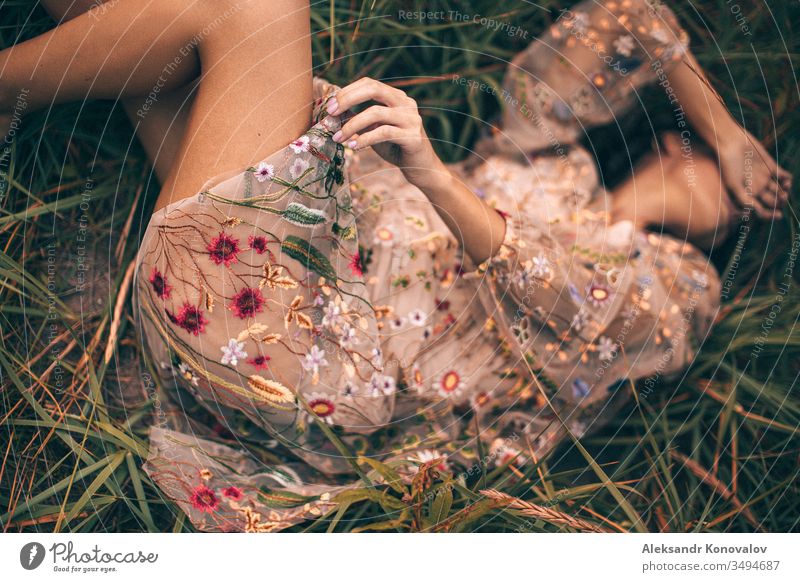 Junge Frau in durchsichtigem Kleid mit Blumen liegt mit dem Arm im Gesicht auf einem Gras Jugendliche romantisch romantische Stimmung frisch Hand Knie Mensch