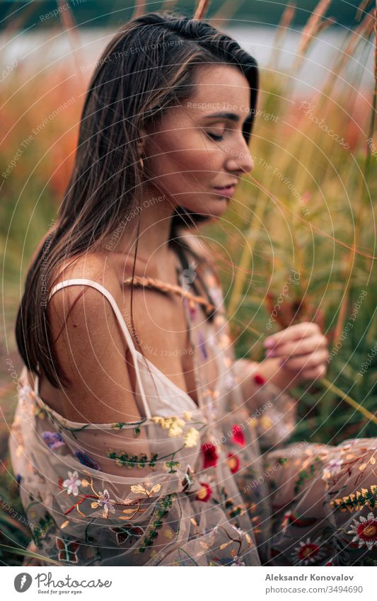 Junge Frau in durchsichtigem Kleid mit Blumen sitzt mit der Weizenähre in der Hand auf einem Gras. Jugendliche romantisch romantische Stimmung frisch Knie